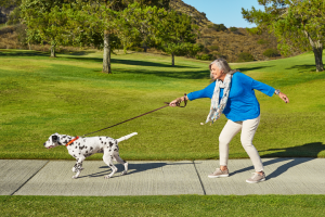 White woman in a park with a dog on a leash pulling her forward